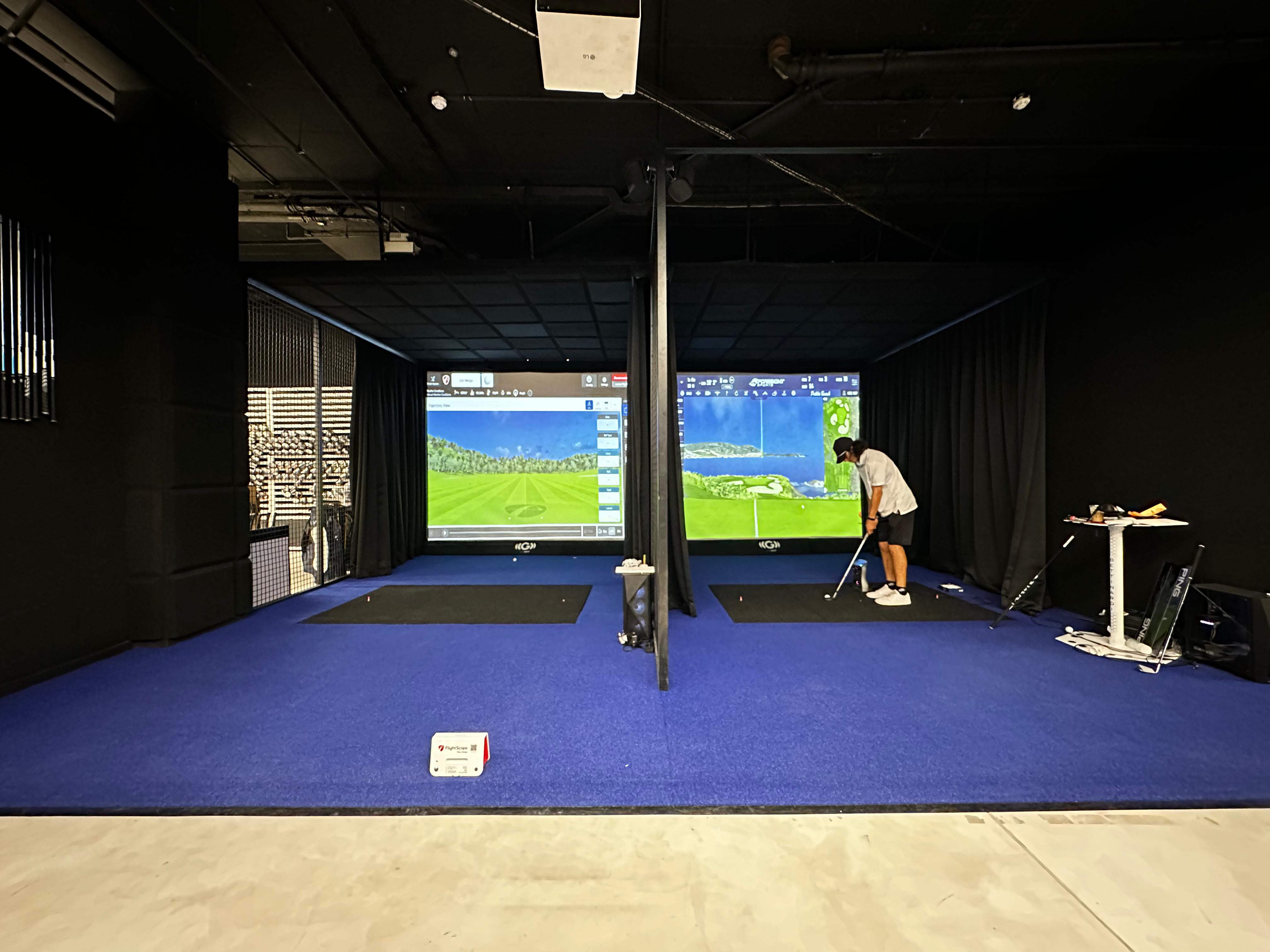 Commercial dual-bay indoor golf installation with blue turf, overhead launch monitors, and golfers practicing in South Africa.
