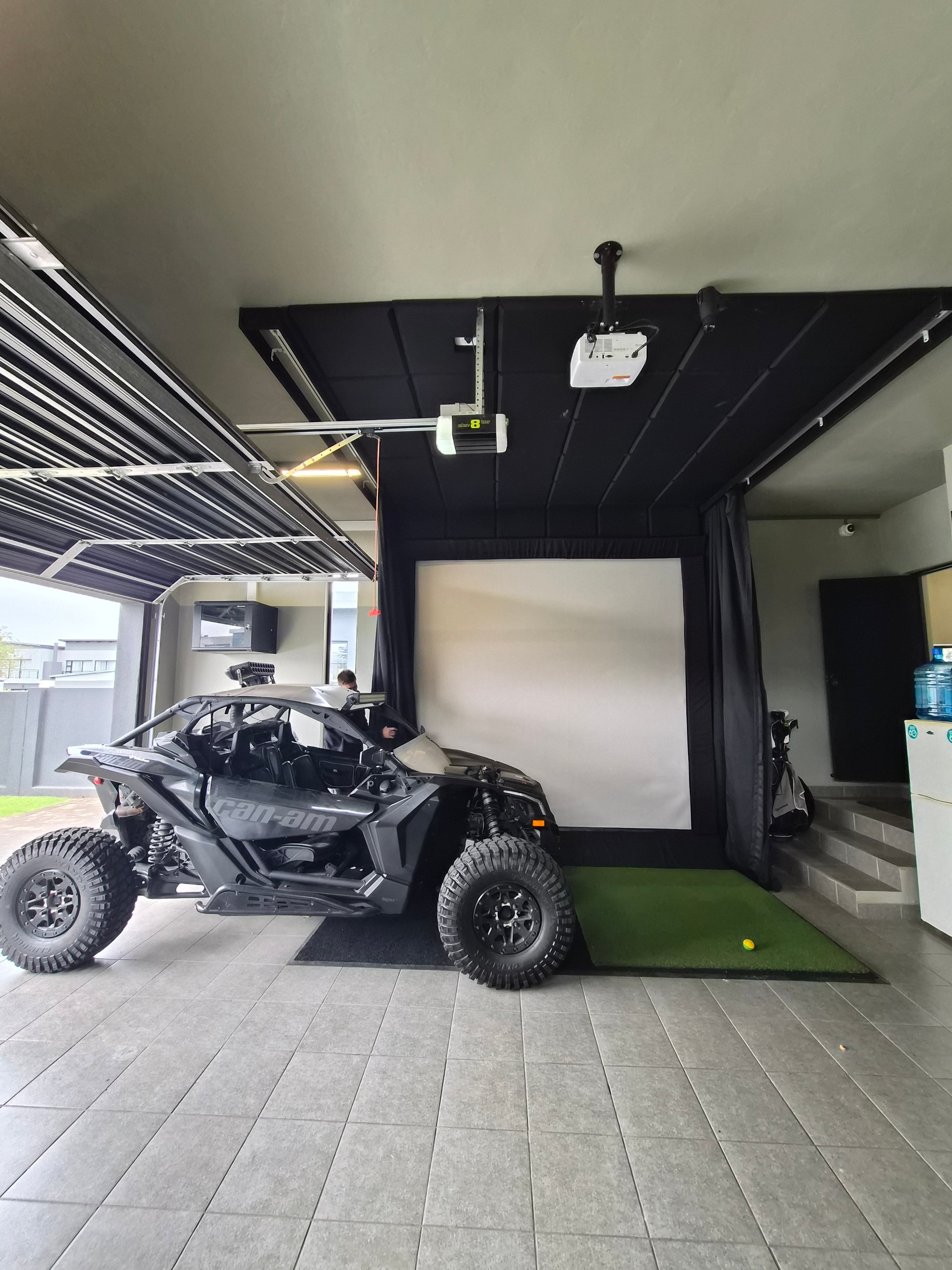 Compact garage golf simulator bay installed alongside an off-road vehicle with retractable side drapes and impact screen.