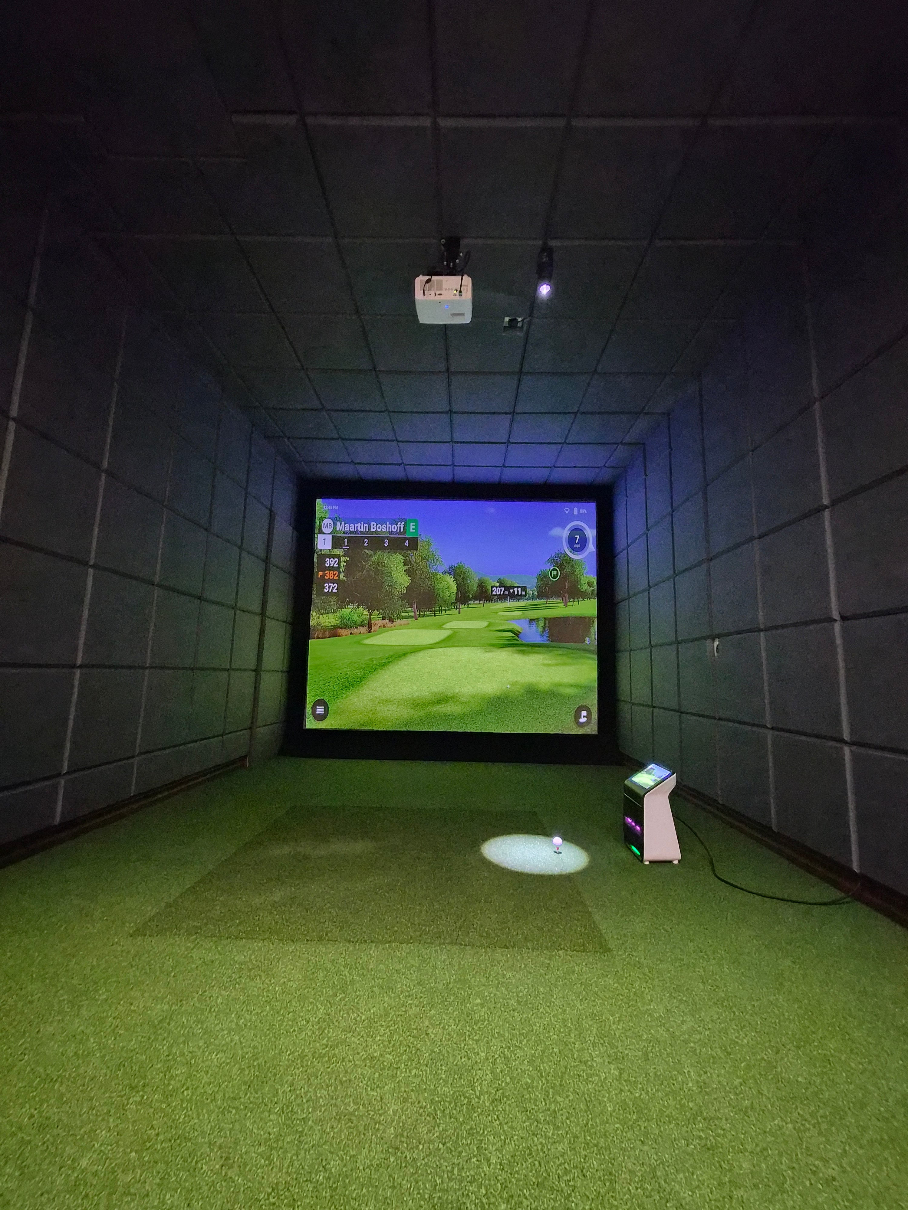 Custom acoustic padded garage golf simulator enclosure with turf hitting mat and high-definition golf simulation software.