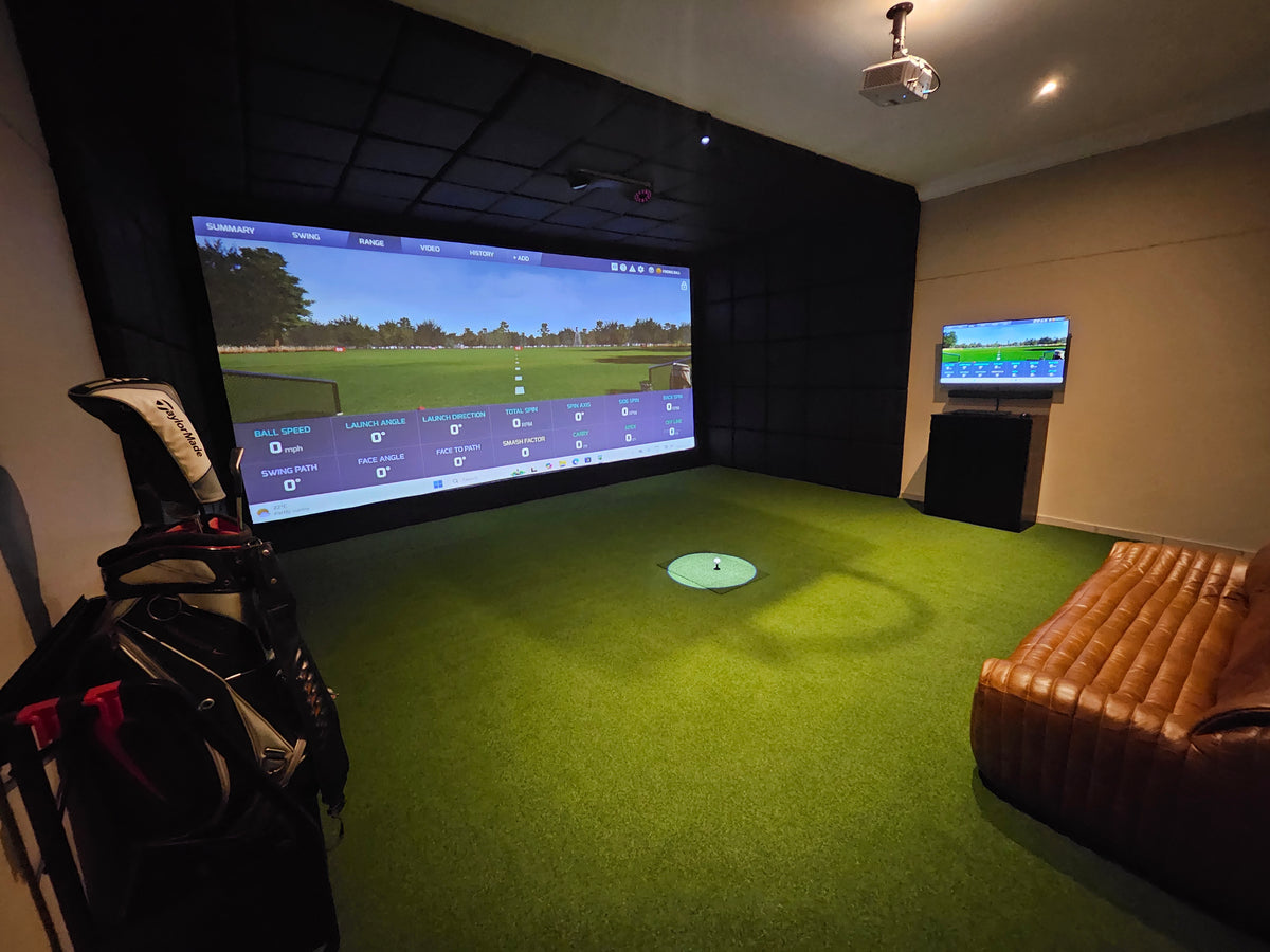 Custom home golf simulator room featuring a high-definition impact screen, full turf flooring, and leather couch seating area.