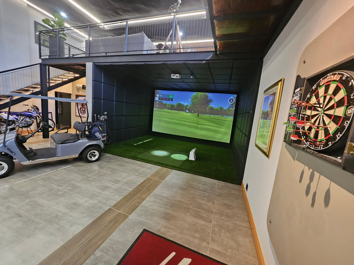 Full-swing commercial golf simulator enclosure featuring a high-impact screen, turf hitting mat, and overhead projector setup.