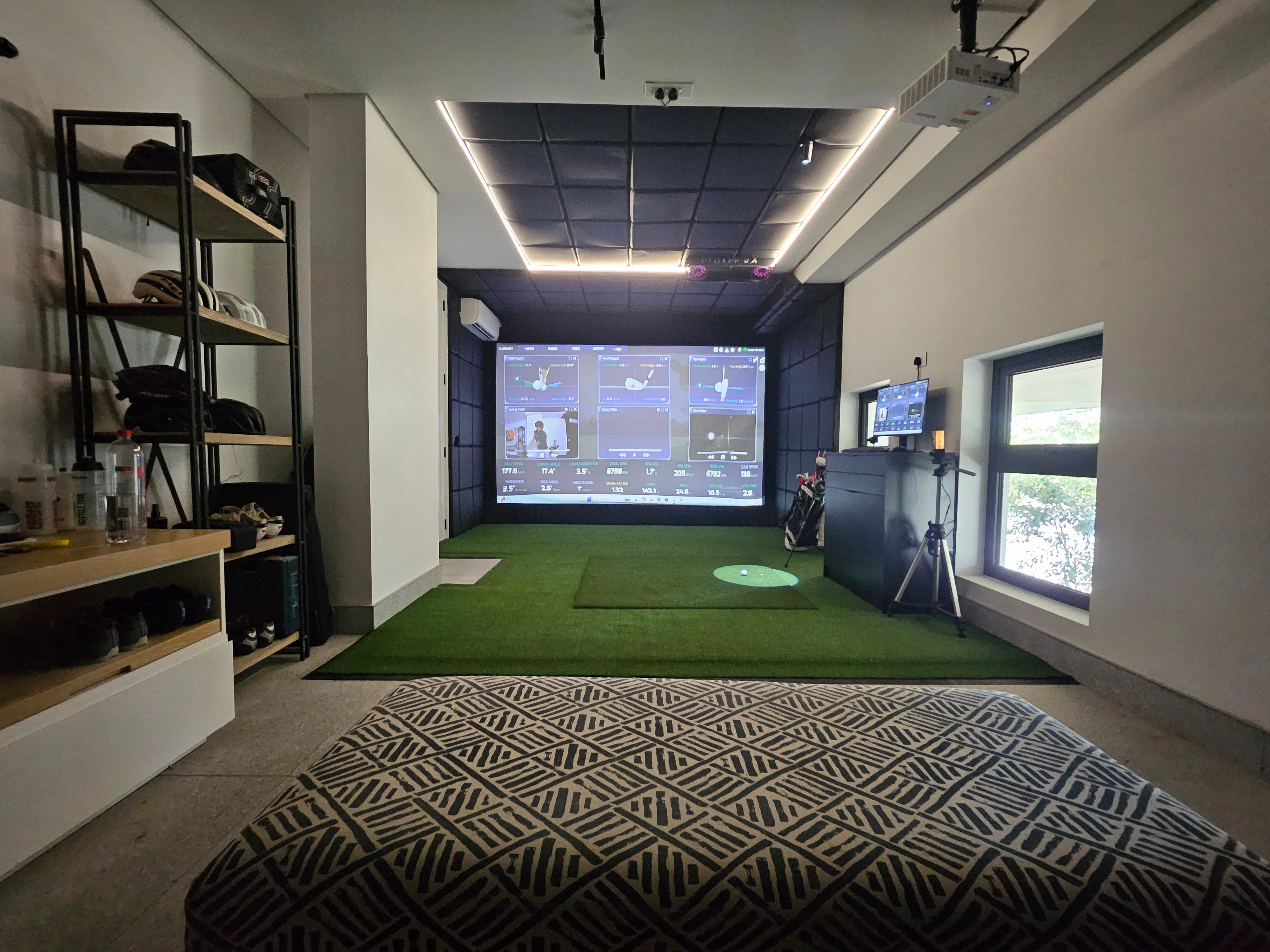 High-end residential golf simulator lounge with L-shaped couch, custom LED enclosure trim, and high-impact projection screen.
