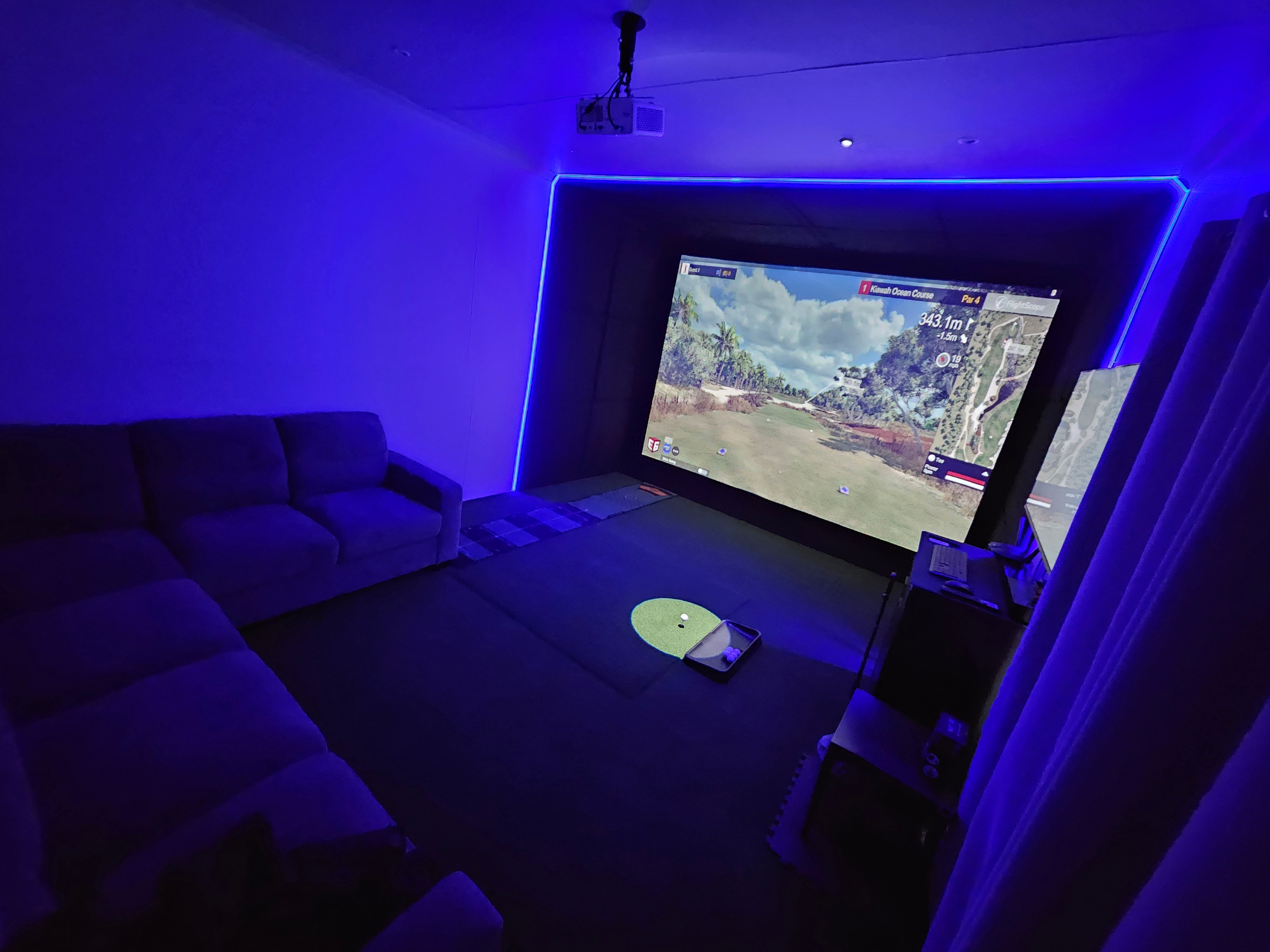 Modern residential indoor golf room setup with custom lighting, acoustic ceiling padding, hitting turf, and dual swing analysis display.
