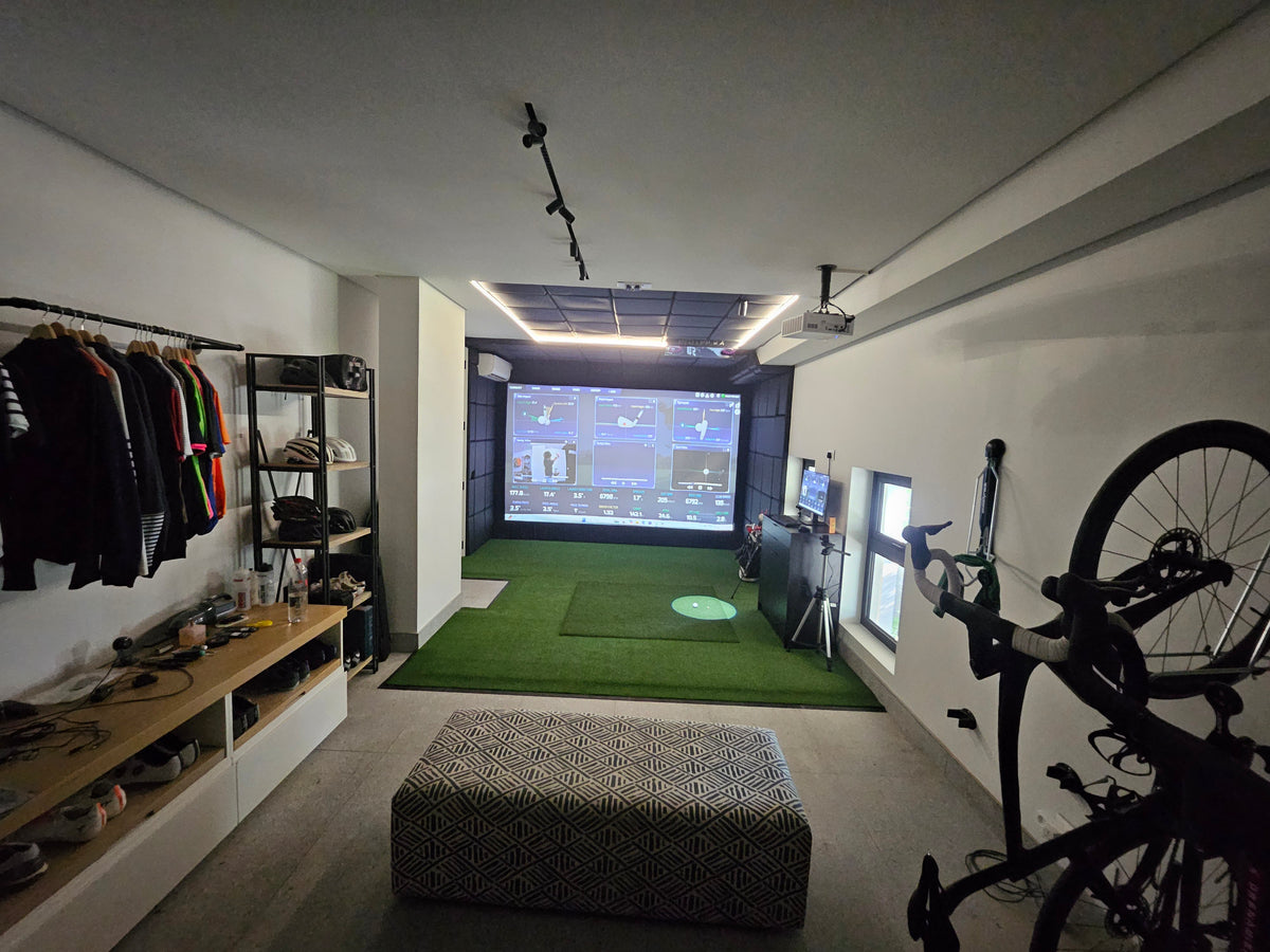 Multipurpose home room combining an indoor golf simulator enclosure with bicycle trainer and custom storage shelving.