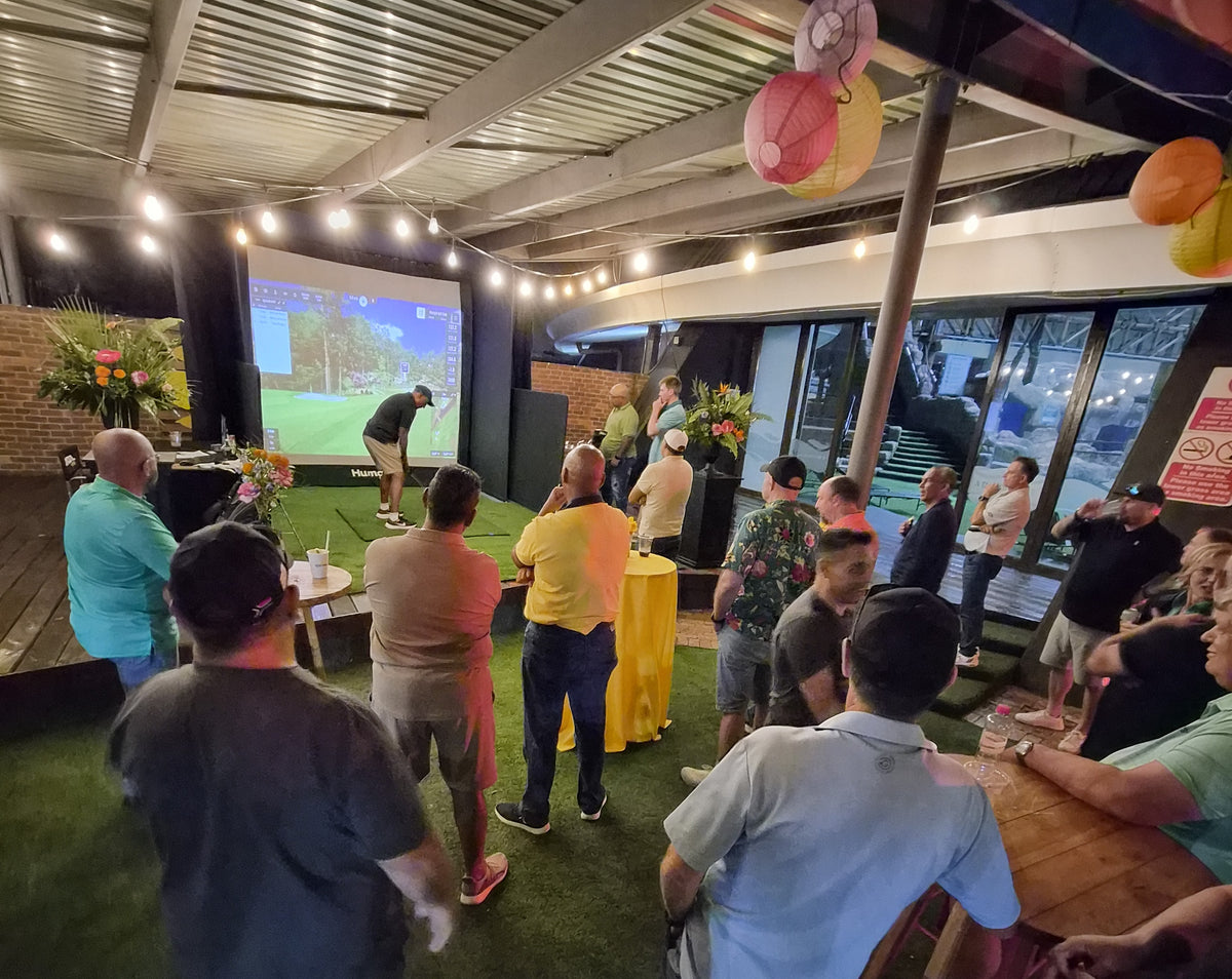 Nighttime event golf simulator hire with overhead string lights and audience