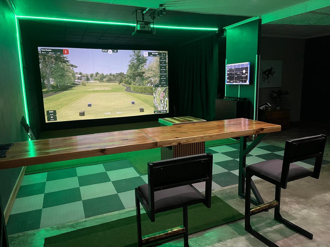 custom commercial golf simulator studio with green ambient LED lighting, high-top seating, and dual analysis monitors.