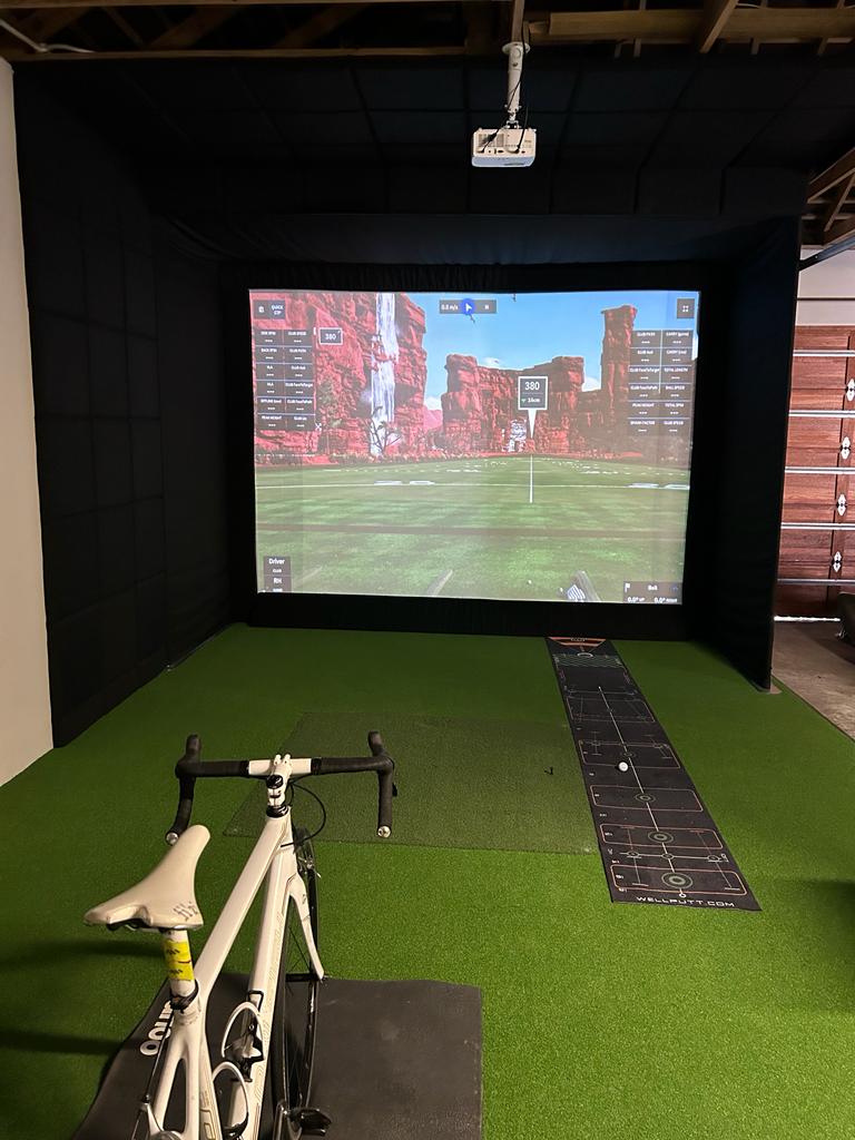 Compact garage golf simulator enclosure with ceiling-mounted projector and indoor putting mat in a residential home.