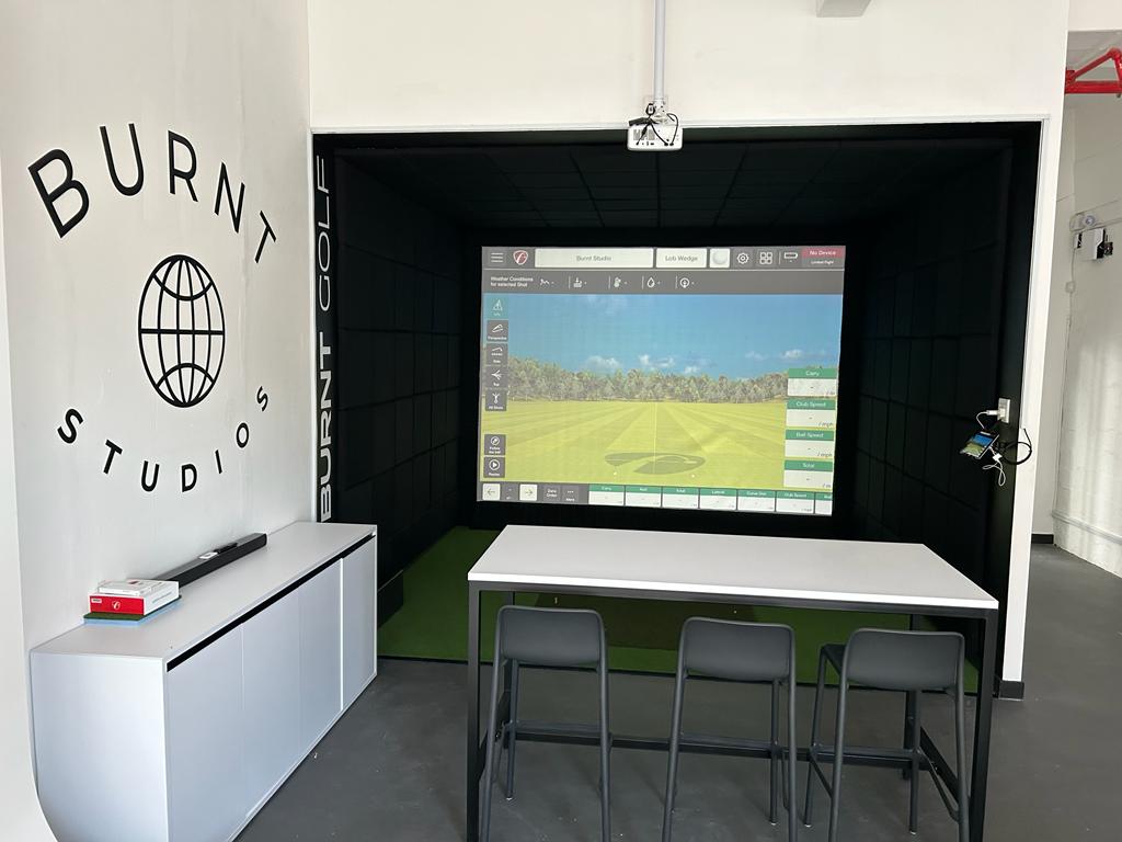 Custom branded commercial indoor golf simulator enclosure at Burnt Studios with precision launch monitor and spectator bar seating.