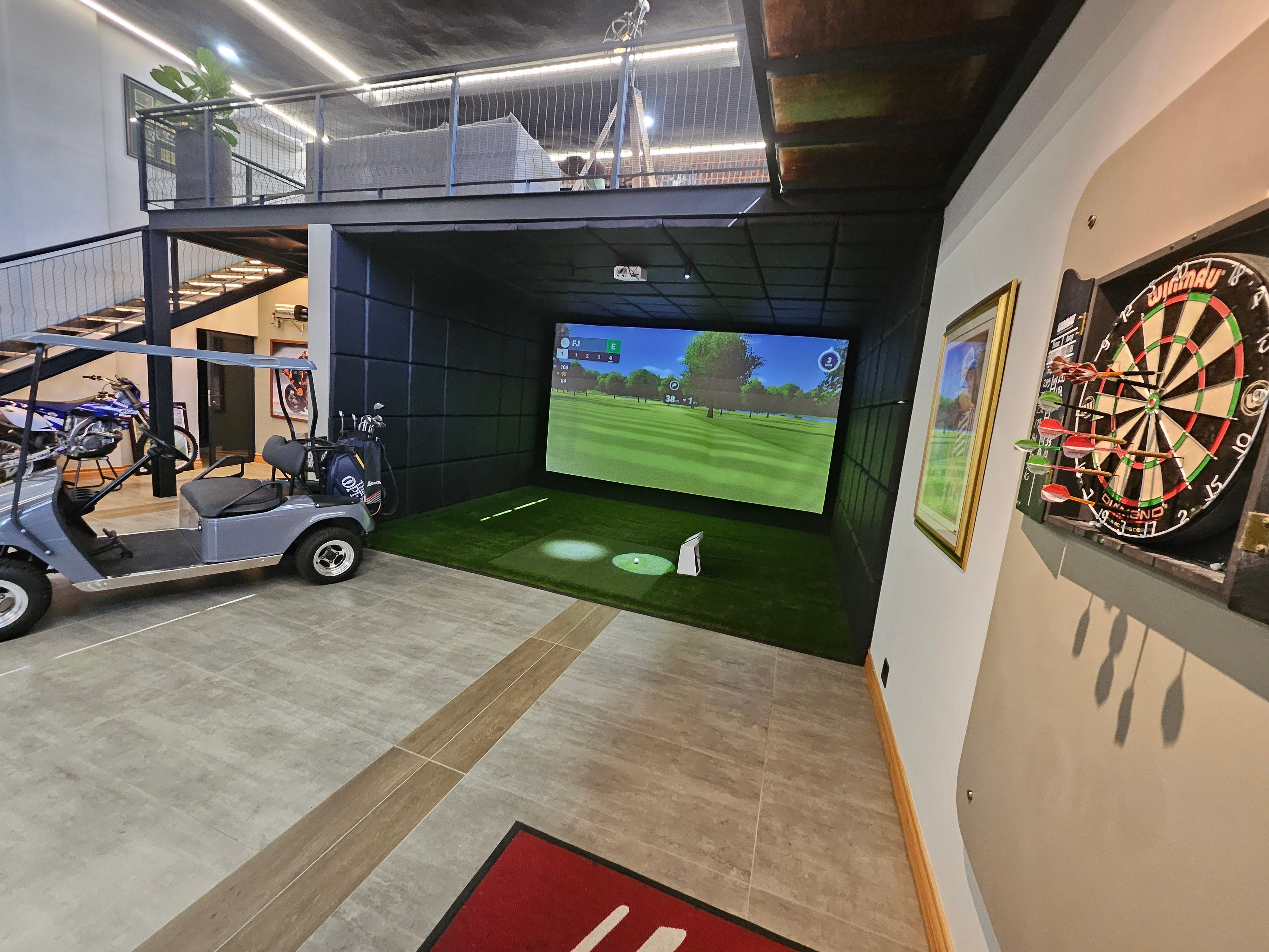 Full-swing commercial golf simulator enclosure featuring a high-impact screen, turf hitting mat, and overhead projector setup.