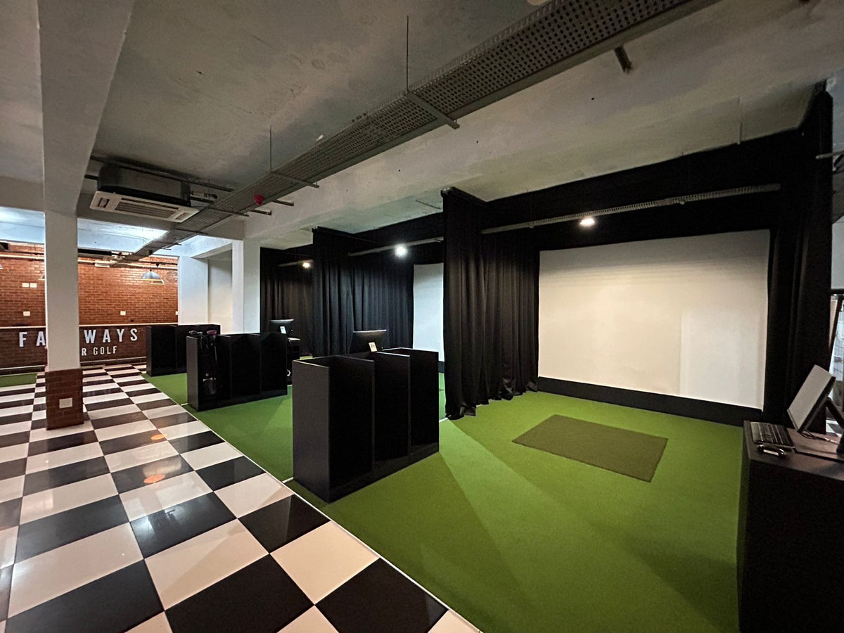 Multi-bay commercial indoor golf facility with black side drapes, high-impact projection screens, and checkered flooring in Hermanus.