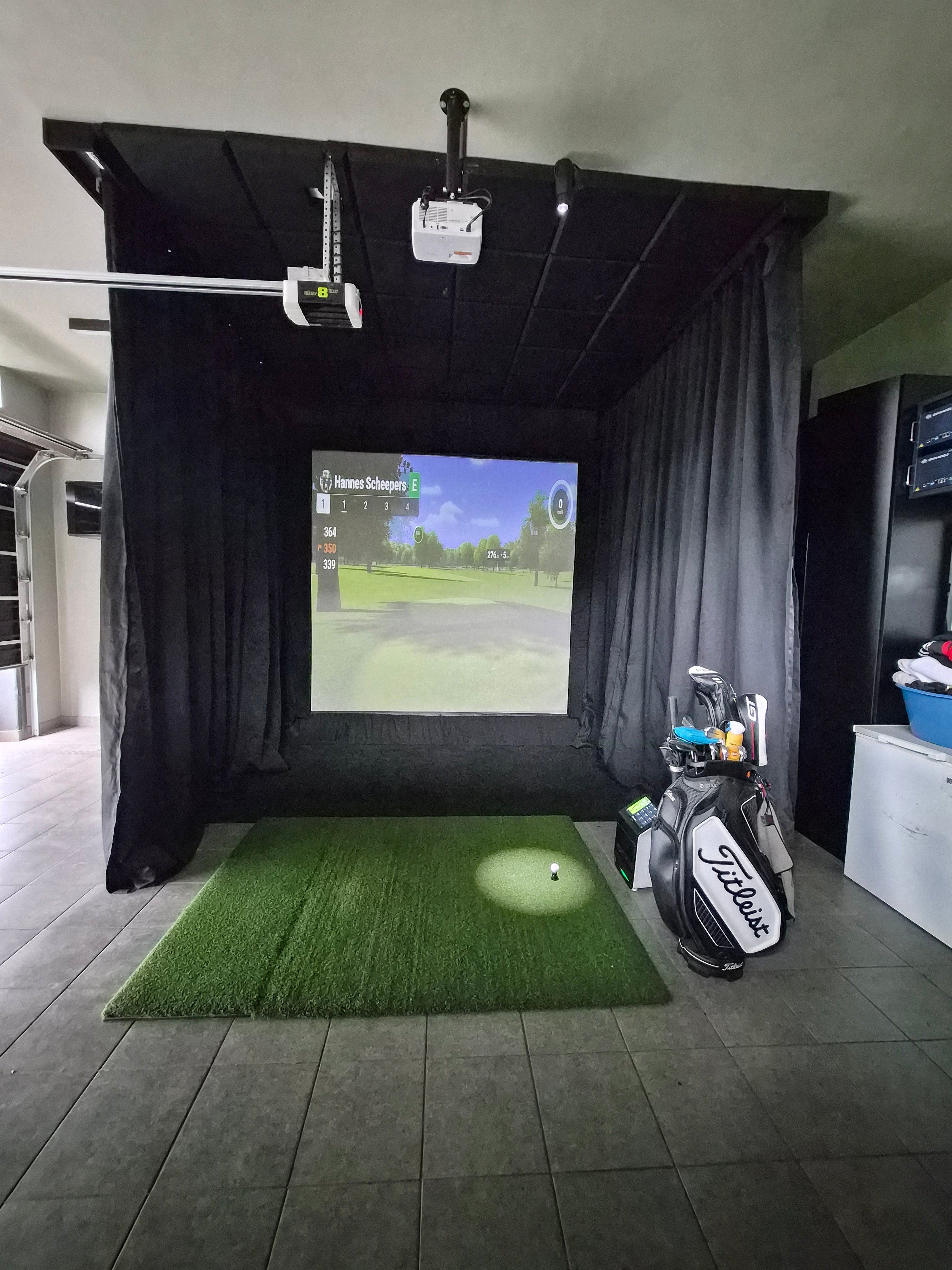Single-car garage golf simulator conversion featuring a black curtain enclosure, hitting mat, and floor-mounted launch monitor.